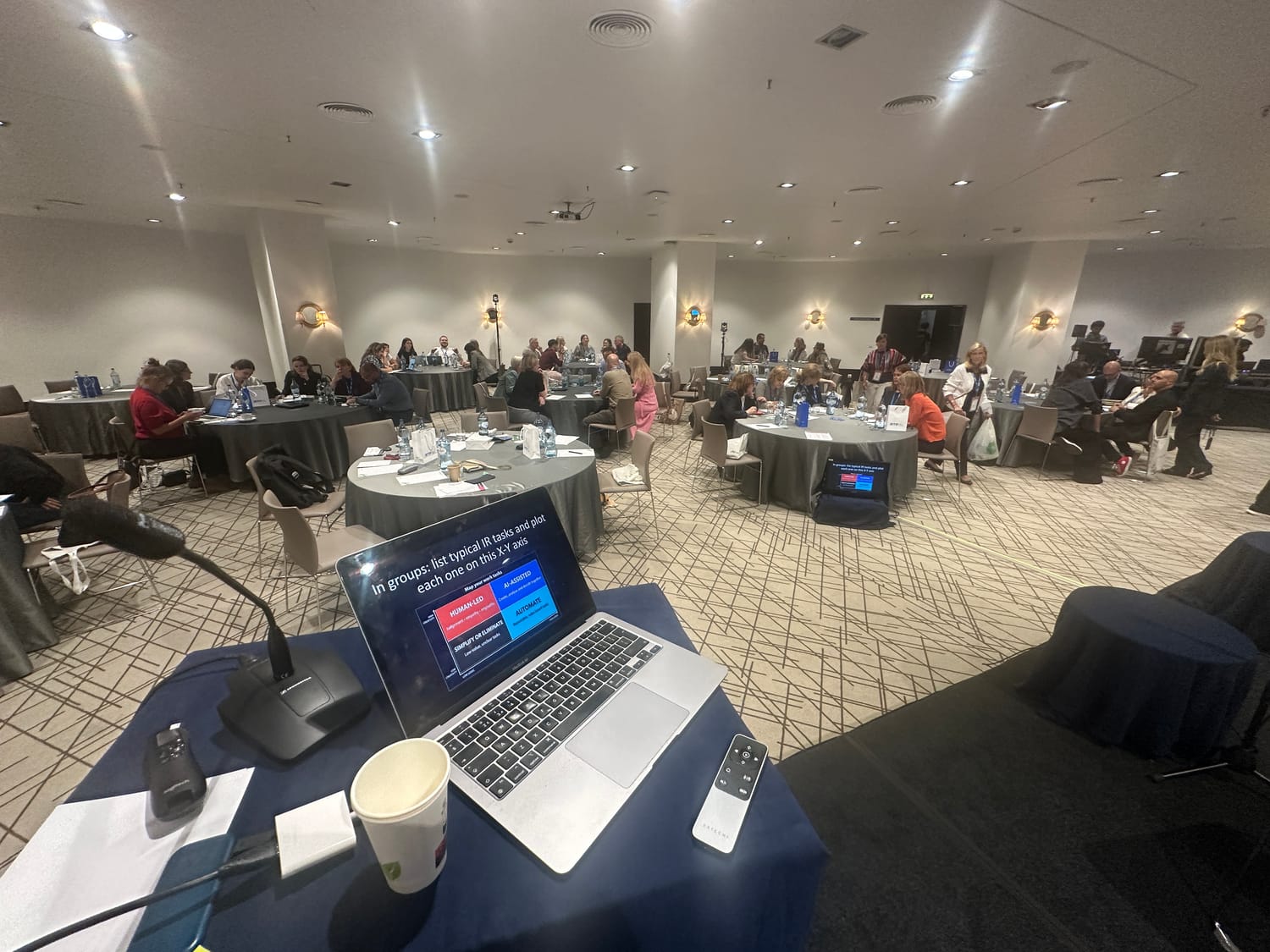 A conference room set up for a session, seen from the presenter’s desk with an open laptop and microphone