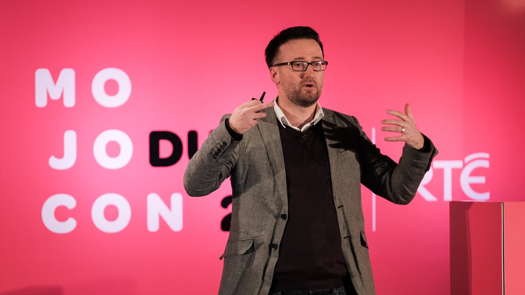 Mark Egan speaking on stage at a conference, gesturing with both hands