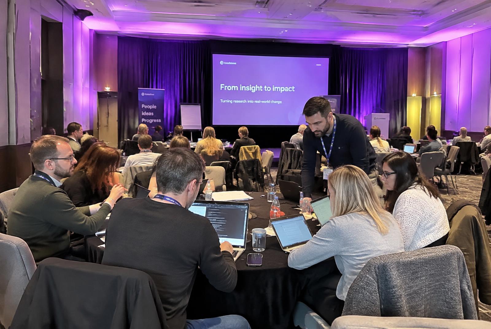 A trainer leaning over a table of participants working on laptops during a workshop
